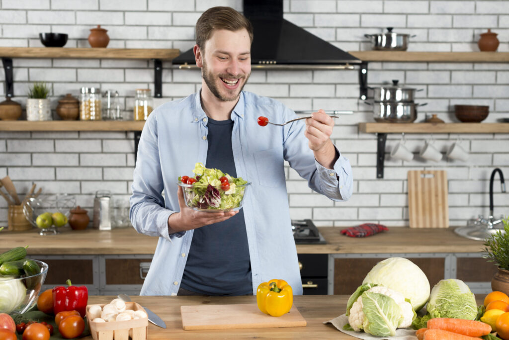 smiling man holding a salad with fresh vegetables on table