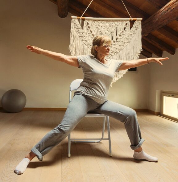 smiling elderly woman stretching arms in chair yoga