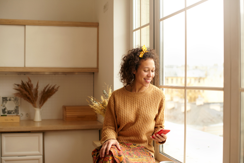 woman smiling by window with phone