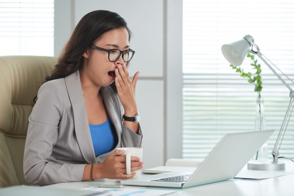 Woman yawning at her desk during early afternoon slump
