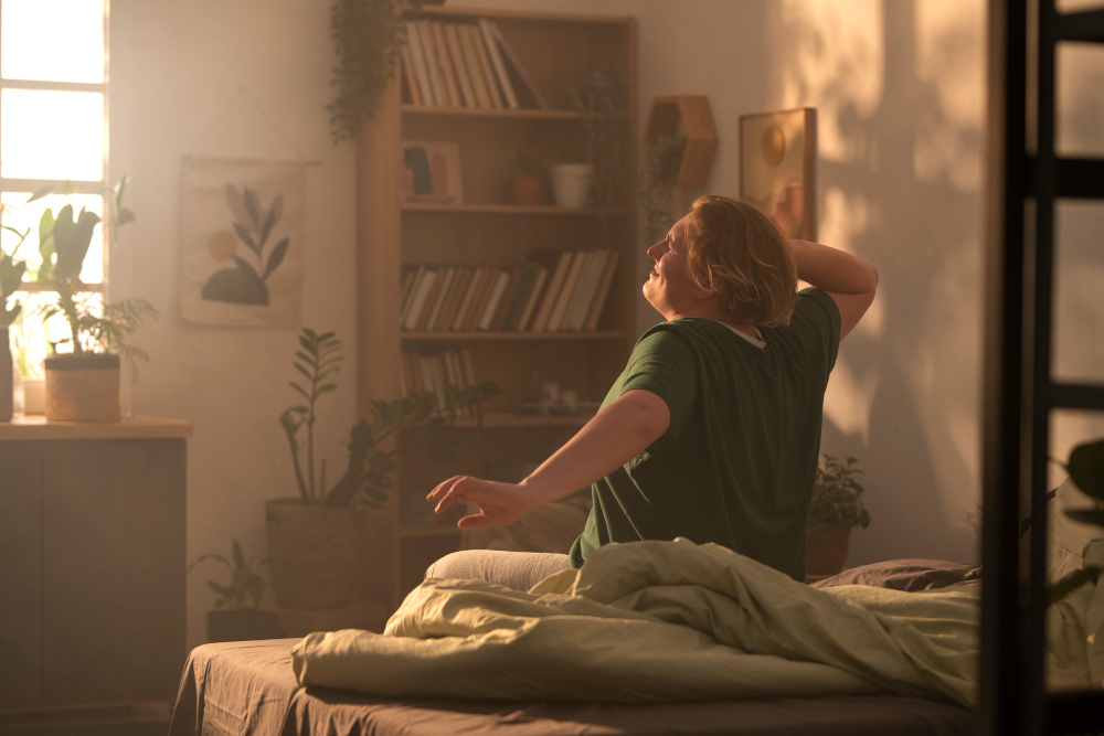 Person stretching arms in bed with sunlight through window