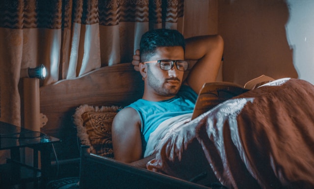 relaxed man lying in bed reading a book